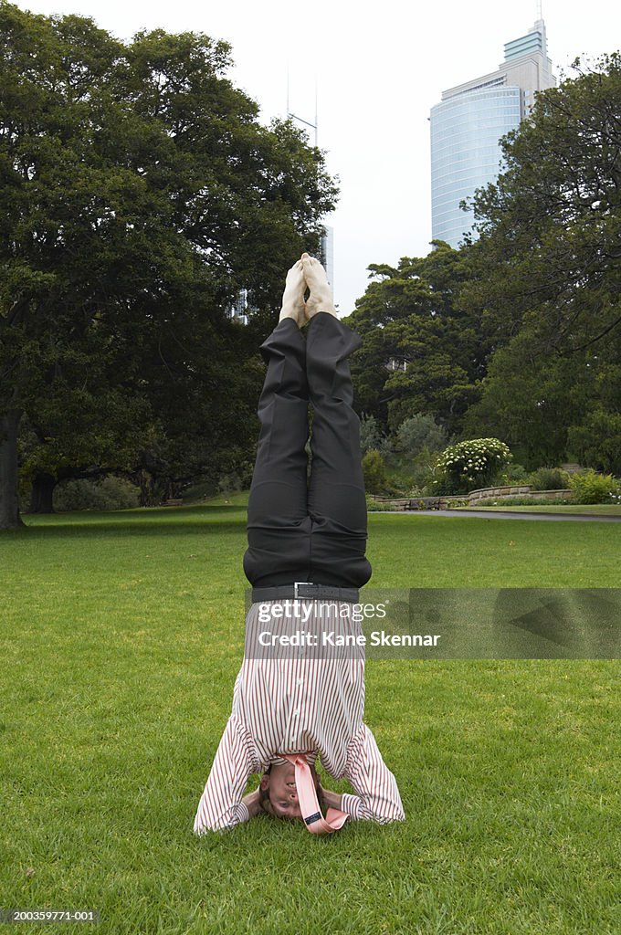 Young businessman doing headstand in park