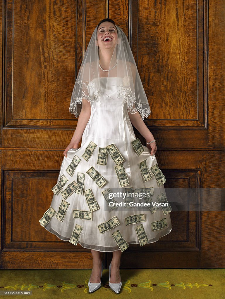 Young bride with banknotes attached to wedding dress, laughing