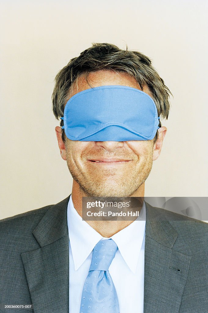 Businessman wearing sleeping mask, smiling, close-up