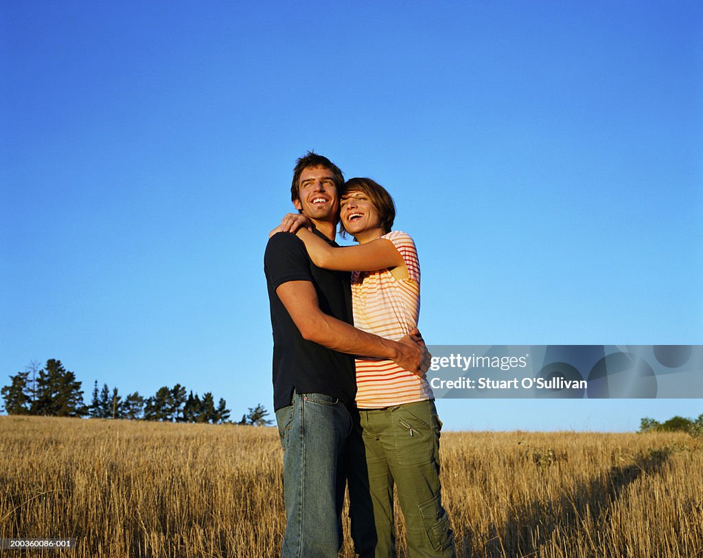 Young couple embracing in field, sunset