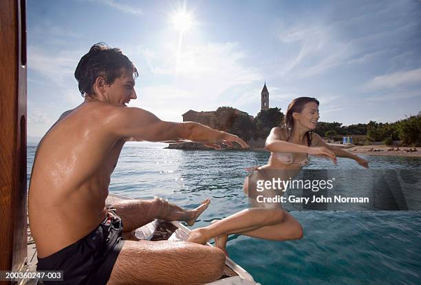 young man pushing woman into ocean from boat, side view - summer press day ストックフォトと画像