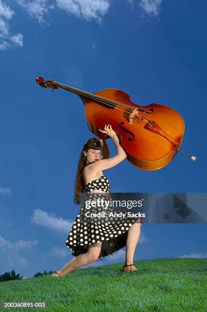 woman holding double bass above head on grassy hillside, portrait - double bass stock pictures, royalty-free photos & images