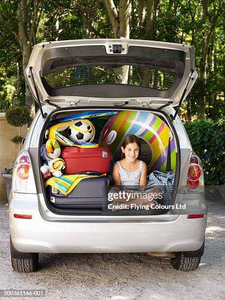 girl (8-10) sitting in boot of car reading amongst luggage, portrait - libri gialli estate foto e immagini stock