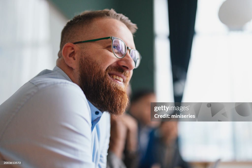 Smiling Bearded Man in Glasses at a Casual Business Meeting