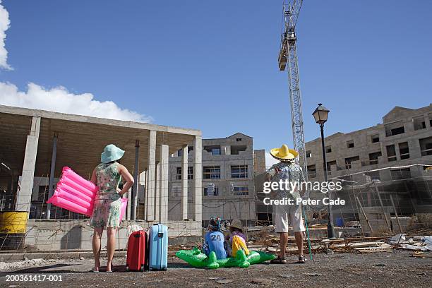 family with suitcases facing building under construction, rear view - negative emotion stockfoto's en -beelden