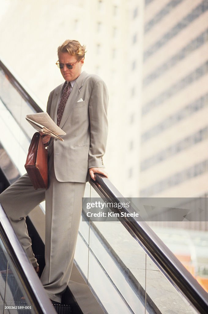 Executive male on escalator reading newspaper