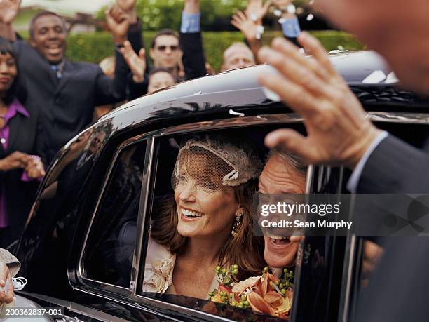 mature newlywed couple looking out of car window, guests cheering - just married car stockfoto's en -beelden