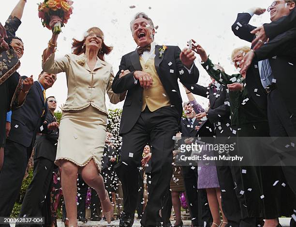 mature newly wed couple running through confetti - bride holding bouquet stock pictures, royalty-free photos & images