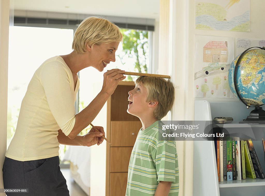 Mother measuring son's (7-9) height against wall, smiling