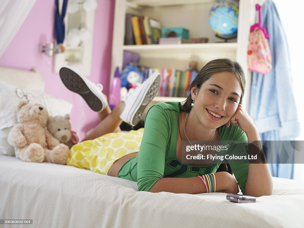 Teenage girl (14-16) lying on bed, smiling, portrait