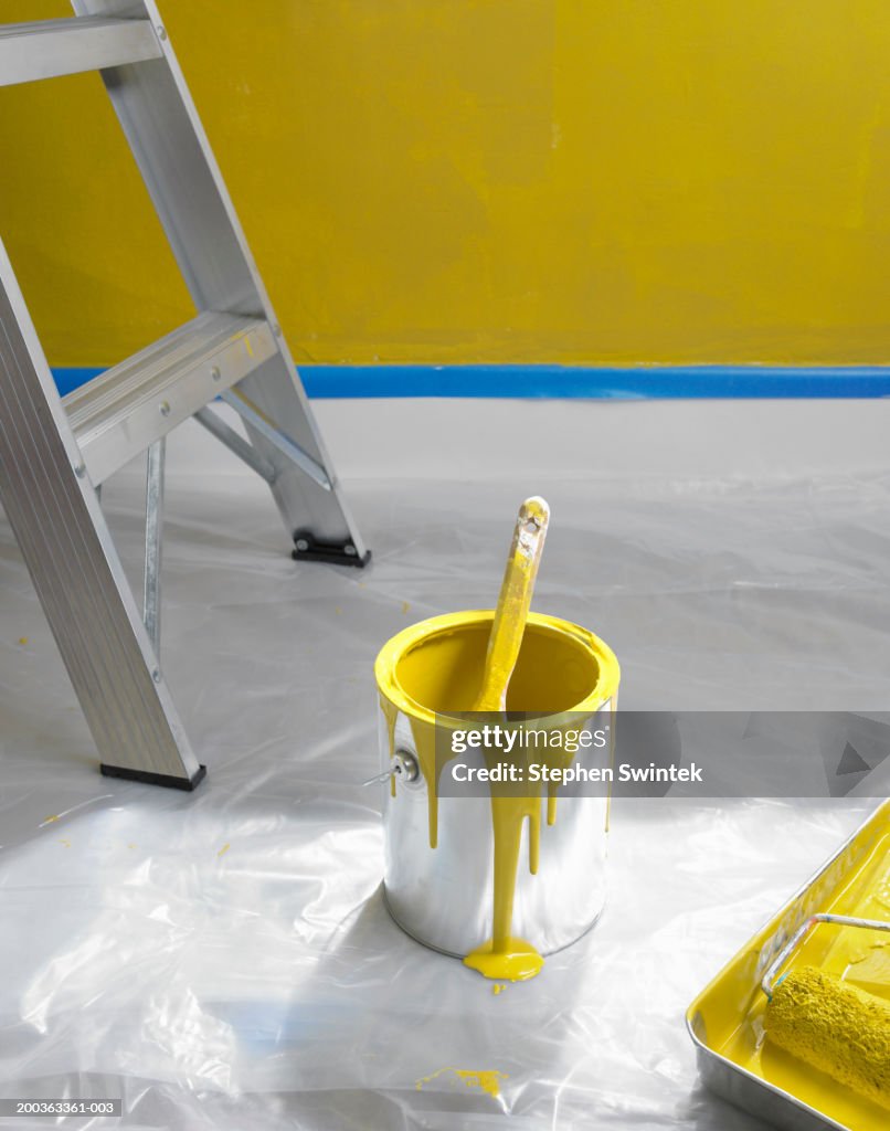 Can of yellow paint and ladder on floor