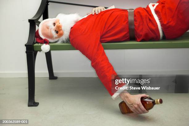 man wearing santa costume, lying on bench, holding whiskey bottle - passed out drunk fotografías e imágenes de stock