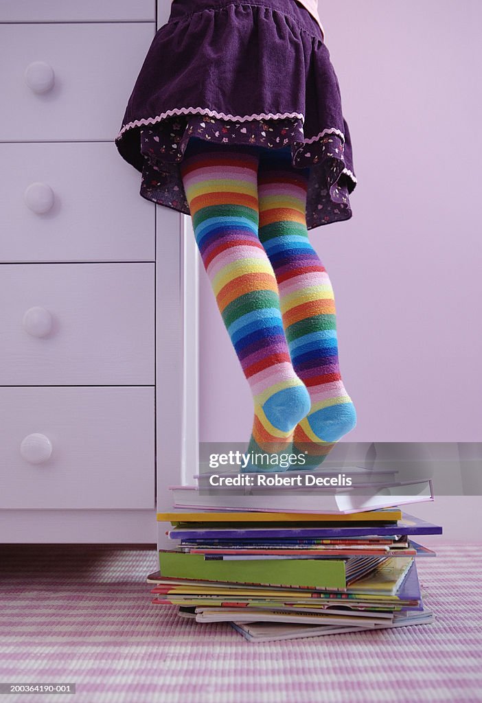 Girl (3-5) standing on tip toes on pile of books, low section