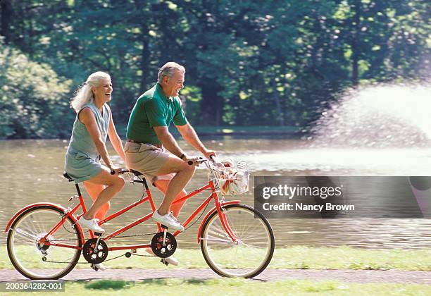 mature couple riding bicycle for two, side view - ciclismo tandem fotografías e imágenes de stock