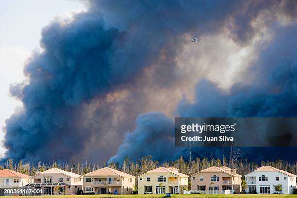 helicopter flying through smoke caused by brush fire behind houses - wildfire stock-fotos und bilder
