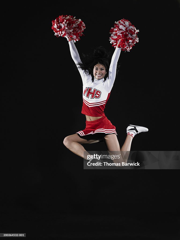 Young female cheerleader jumping in midair, arms raised
