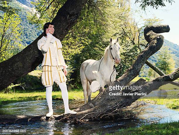 young man in prince costume using cell phone beside horse and river - prince charming stockfoto's en -beelden