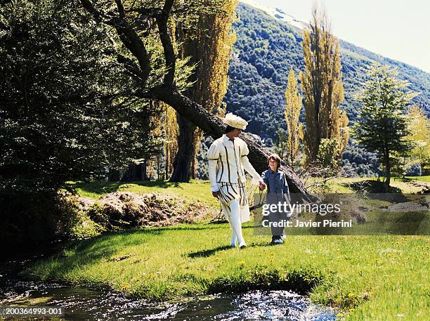 boy (8-10) and young man in prince costume walking across field - prince charming stock-fotos und bilder