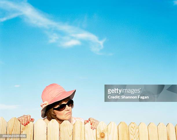 mature woman looking over fence - neugierde stock-fotos und bilder