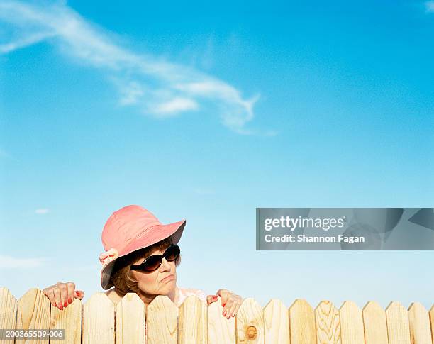 mature woman looking over fence - bad neighbor stock pictures, royalty-free photos & images