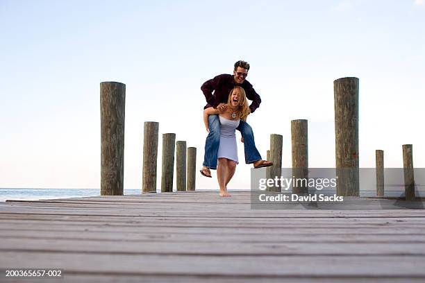 woman giving man piggy back ride on dock, smiling - nassau bahamas stock pictures, royalty-free photos & images