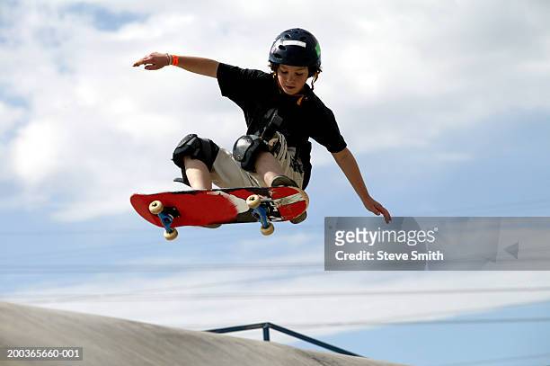 boy (9-11) performing jump on skateboard, low angle view - skating stock pictures, royalty-free photos & images