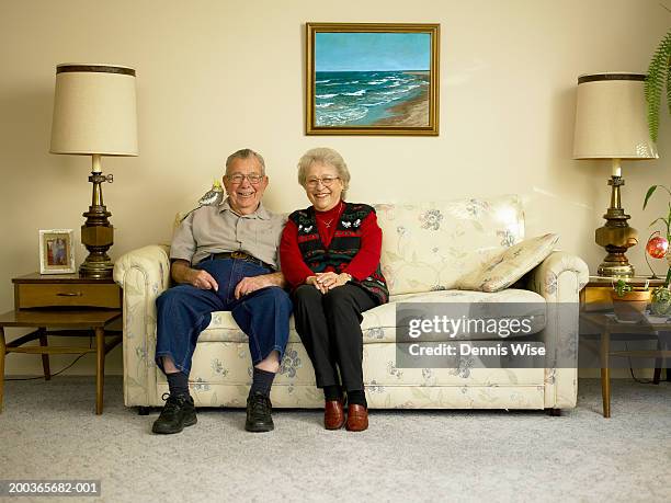 senior couple sitting on sofa, bird on man's shoulder, portrait - tavolino di servizio foto e immagini stock