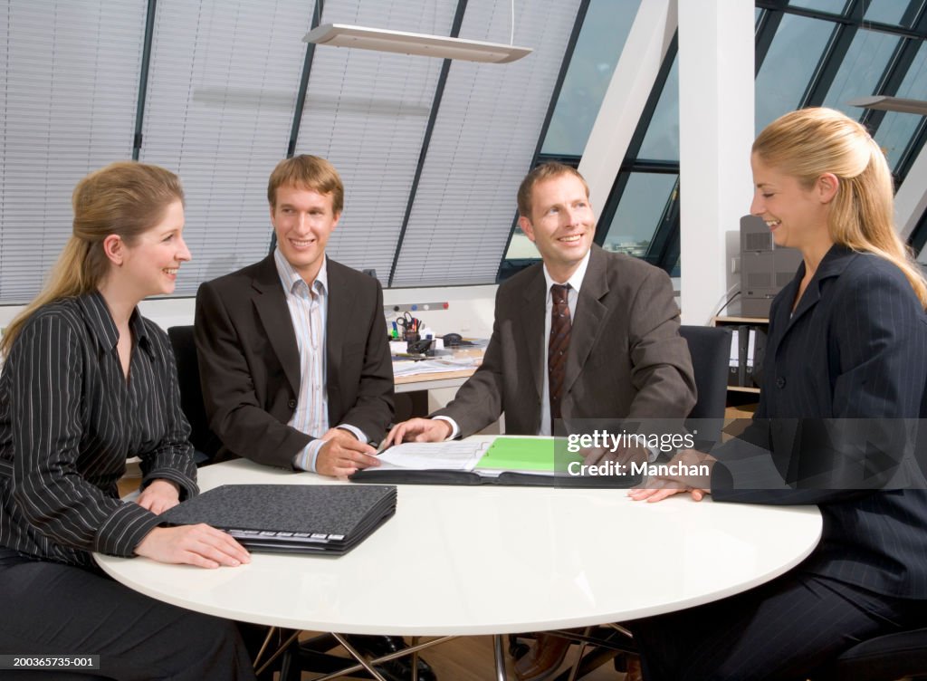 Four businessmen and businesswomen in meeting, smiling