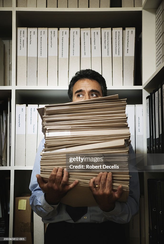 Mature businessman holding stack of files, looking sideways