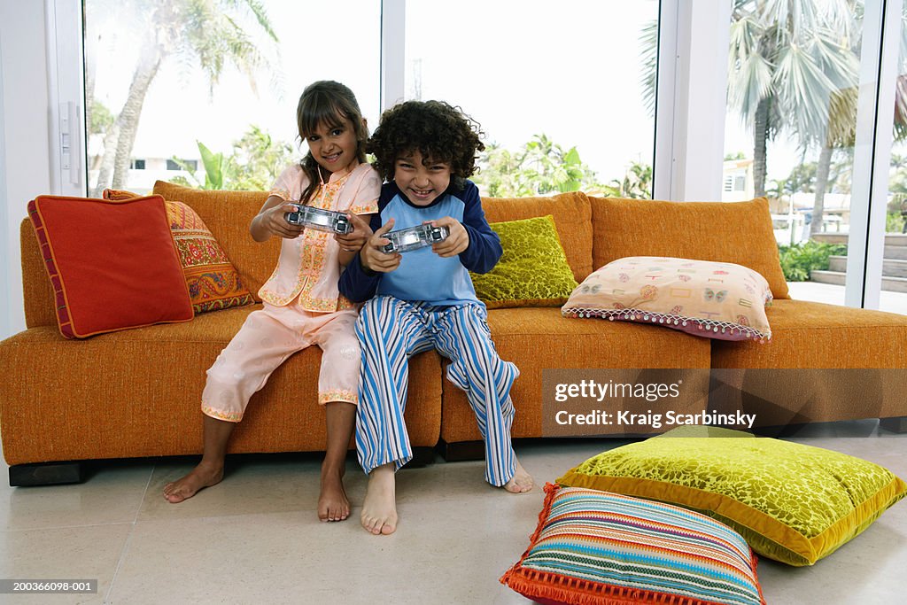 Brother and sister (8-10) playing video game, smiling