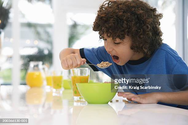 boy (8-10) at table, eating cereal - boy eating cereal foto e immagini stock