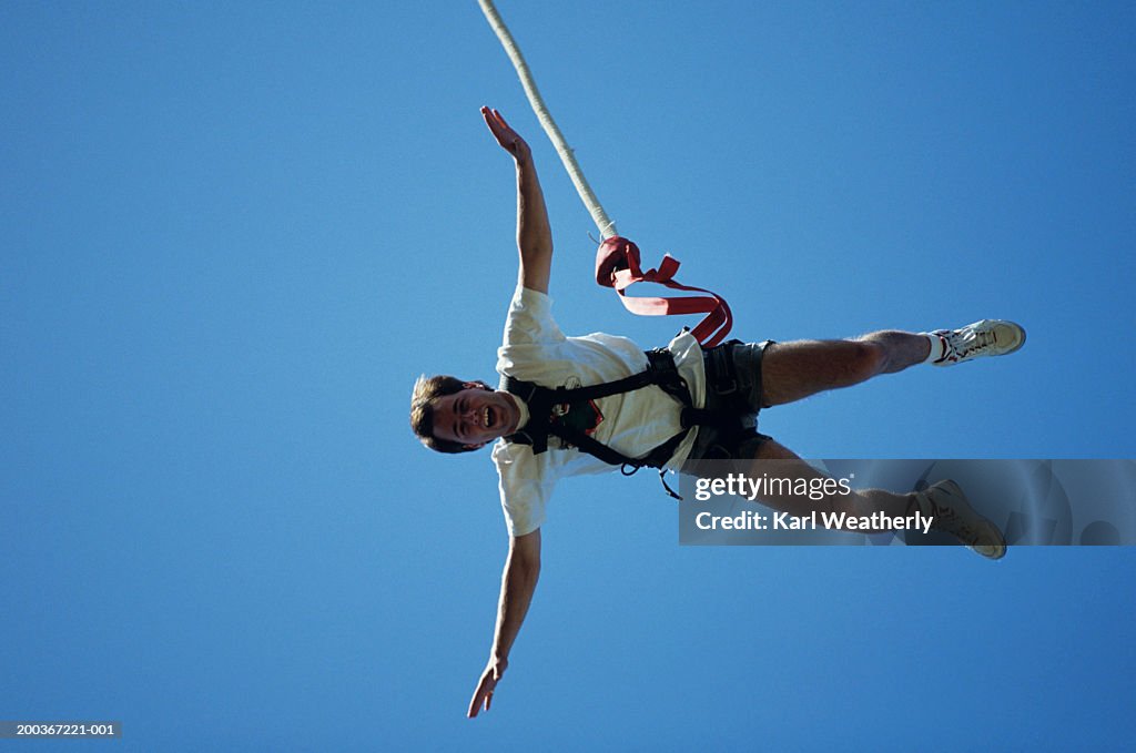 Man bungee jumping, seen against blue sky, view from below