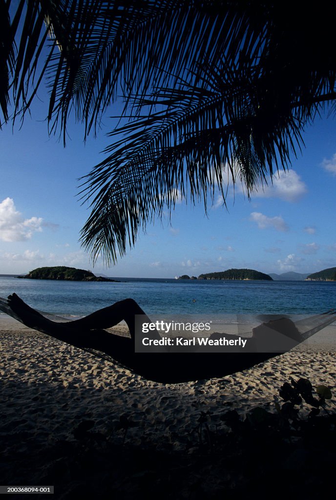 Silhouette of woman lying on hammock on beach