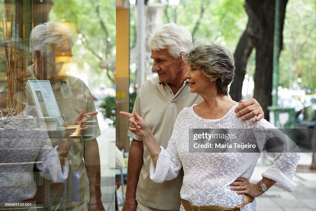 Senior couple looking in shop window, woman pointing