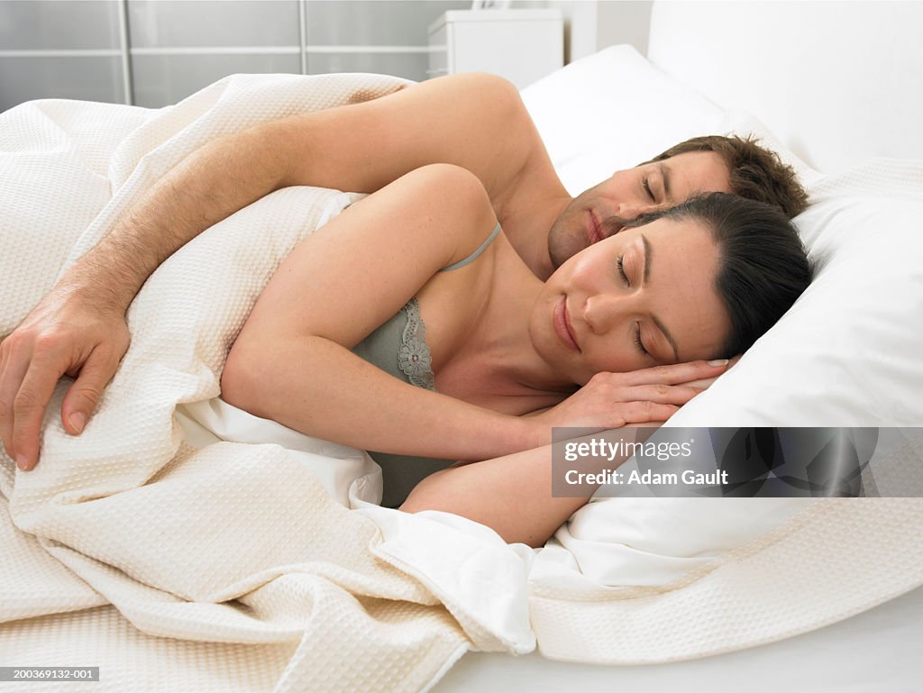 Couple asleep in bed, man embracing woman