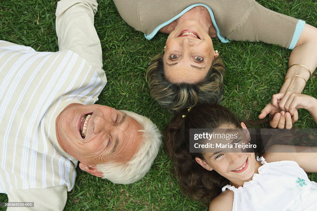 Grandparents and granddaughter (8-10) lying on grass, smiling