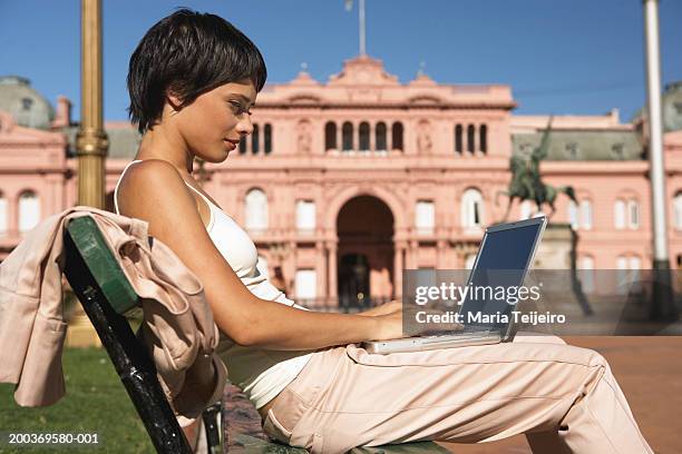 young woman sitting on bench using laptop, side view - cami parker bildbanksfoton och bilder