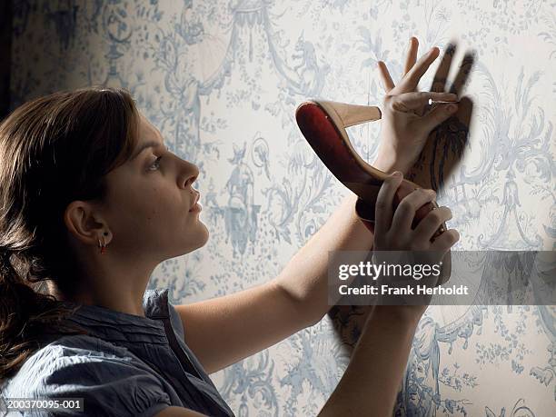 young woman hammering nail into wall with shoe - pieno di risorse foto e immagini stock