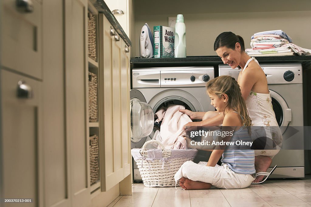 Girl (7-9) helping mother with laundry, smiling