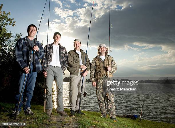 four men holding fishing rods by lake, portrait, low angle view - fishing rod stock-fotos und bilder