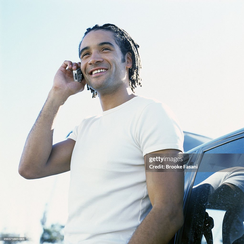 Man using mobile phone, leaning against car