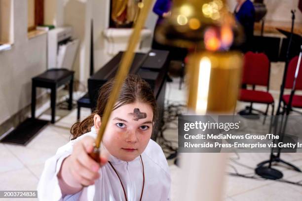 Riverside, CA Altar server Liza Corr seen with a cross of ashes on her forehead, extinguishes a candle Wednesday, Feb. 14 during an Ash Wednesday...