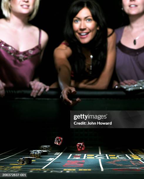 three women leaning on gaming table one throwing dice, smiling - casino dice stock pictures, royalty-free photos & images