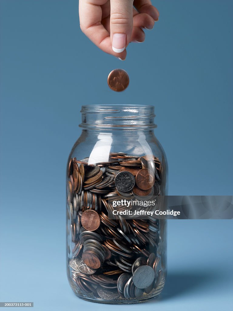 Woman dropping coin into jar close-up