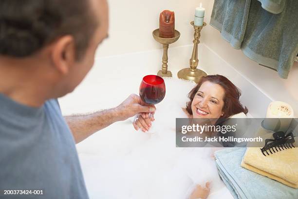 high angle view of a mature man giving a mature woman a glass of wine in a bathtub - indulgence stock pictures, royalty-free photos & images