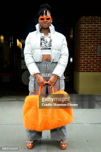 Guest wears a light grey abbreviated puffer, a cropped t-shirt, coated grey wide-leg carpenter pants, an oversized orange teddy faux fur dufflebag,...