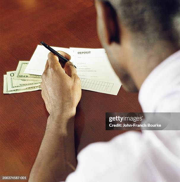 man filling out bank deposit slip. rear view, close-up (focus on hand) - bank deposit slip fotografías e imágenes de stock