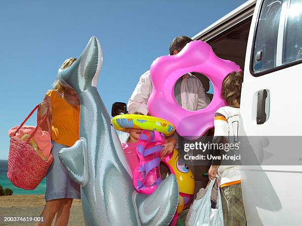 family holding inflatable toys by car outdoors - beach bag stock-fotos und bilder