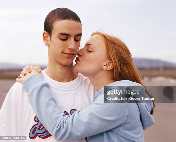 teenage couple (15-17) embracing, girl preparing to kiss boy's cheek - boyfriend stockfoto's en -beelden