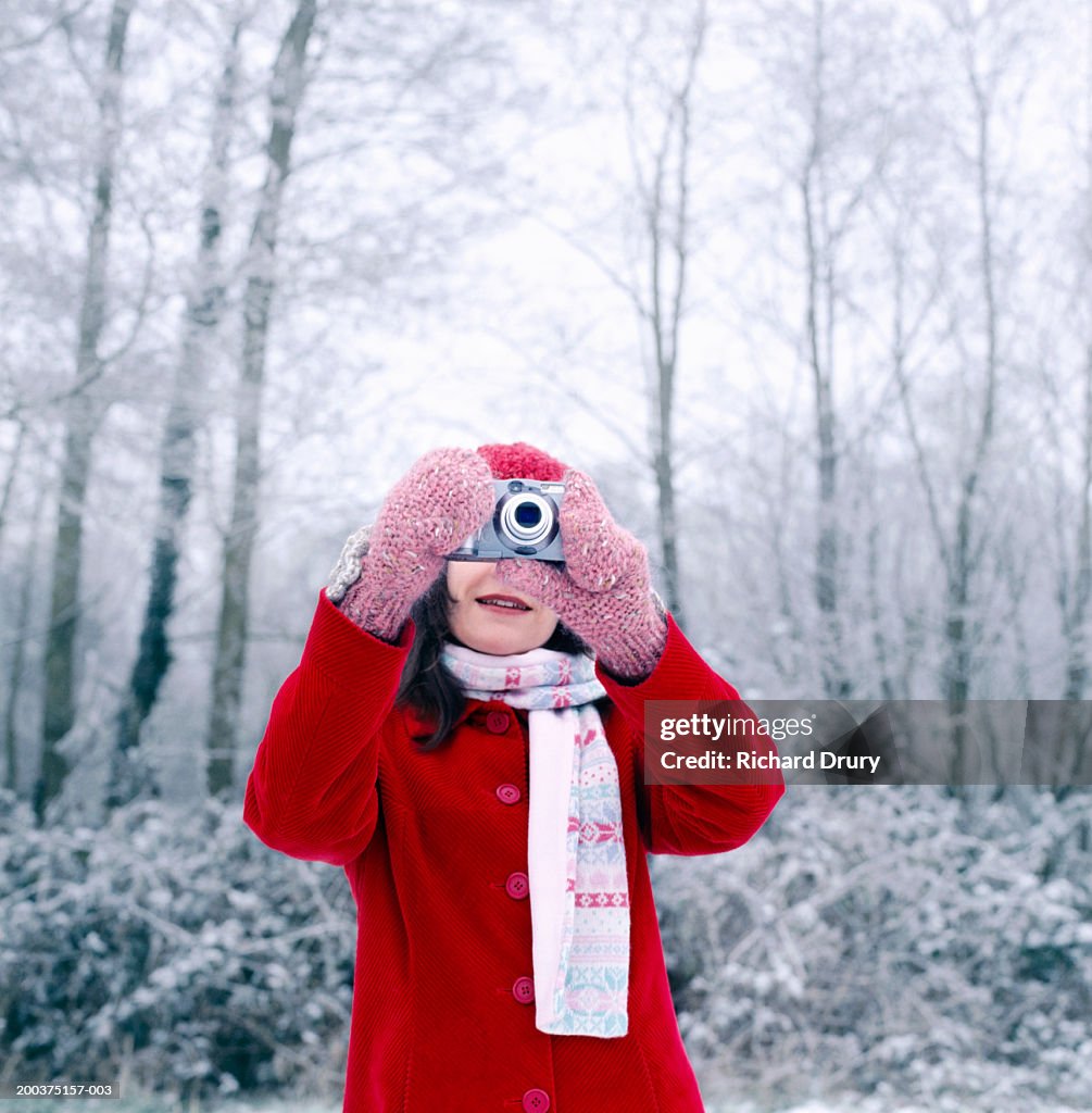 Woman taking photograph outdoors, camera obscuring face, winter